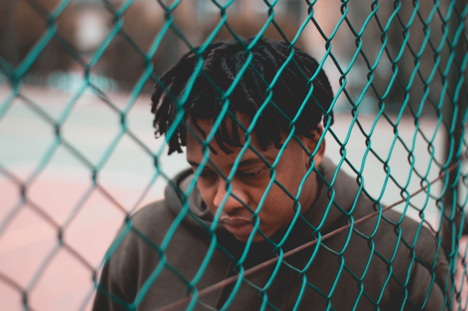 man in gray hoodie standing beside chain link fence